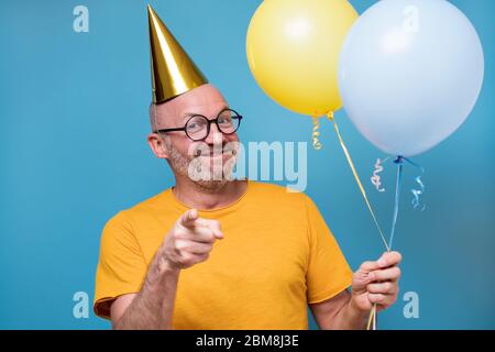 guy avec des lunettes tenant des ballons, souriant et pointant avec le doigt vers vous. Banque D'Images