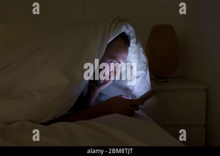 Dépendance mobile, nomophobie, insomnie, concept de trouble du sommeil. Homme ennuyé à discuter et surfer sur Internet avec smartphone tard dans la nuit, allongé sur être Banque D'Images