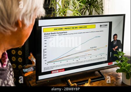 Une femme regardant le couronnement télévisé Downing Street Briefing avec un graphique des taux de mortalité mondiaux comparant les pays touchés. Banque D'Images