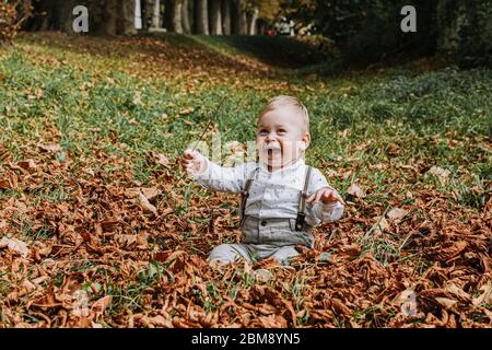 un garçon de 1 an mignon dans une veste jaune élégante souriant et assis sur l'herbe dans le parc Banque D'Images