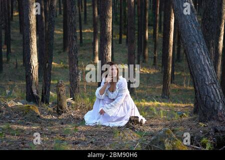 fille dans une robe blanche dans la forêt au coucher du soleil Banque D'Images