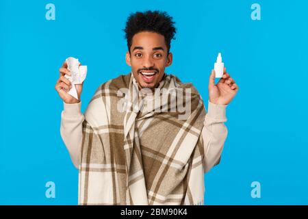 Guy joyeux de se sentir mieux après l'utilisation des médicaments prescrits par un médecin, le port de couverture comme sont tombés malades, attrapé froid ou la grippe, holding spray nez bouteille et Banque D'Images