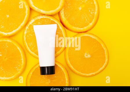 Produit naturel de soin de la peau en vitamine c avec des tranches de fruits d'orange juteux frais sur fond jaune. Crème hydratante, mousse pour le visage, lotion pour le corps au citron Banque D'Images