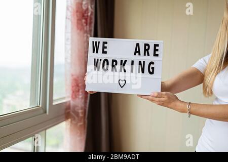 Femme tenant une visionneuse avec du texte que nous travaillons. Fin de la quarantaine Covid-19. Hôtel, restaurant, café, magasin local, propriétaire du service accueillant les clients après Banque D'Images