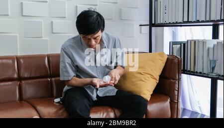 Un homme asiatique âgé est assis sur le canapé et mange des médicaments pour traiter la maladie à la maison. Banque D'Images