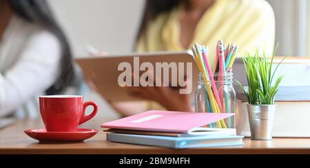 Cafetière en céramique rouge et petit plat sur un bureau en bois entouré d'un carnet, d'une pile de livres. Plante en pot, crayons dans un vase en verre Banque D'Images