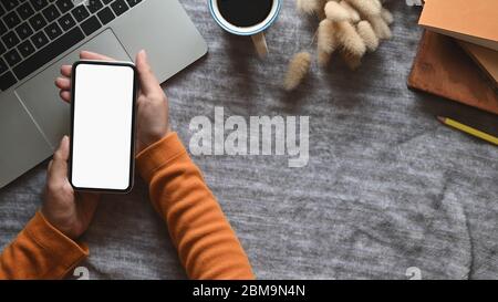 Vue de dessus image des mains tenant un smartphone blanc écran sur ordinateur portable, vieux livres, tasse de café et herbe sauvage qui se mettent au travail Banque D'Images