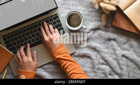 Vue de dessus d'un espace de travail confortable. De la main dactylographiée sur écran vierge ordinateur pile de livres et tasse de café sur table de travail. Banque D'Images