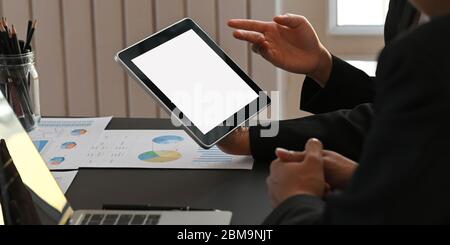 Image rognée des professionnels travaillant avec une tablette, un ordinateur portable et des graphiques tout en étant assis à une table de réunion noire au-dessus de M. Banque D'Images