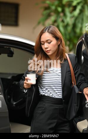 Photo d'une femme d'affaires attirante qui sort de sa voiture alors qu'elle était arrivée sur son lieu de travail, en plein air ensoleillé comme arrière-plan. Banque D'Images