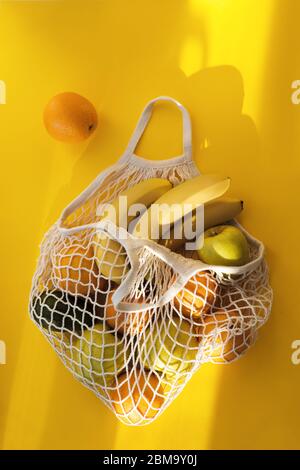 Oranges, bananes, pommes, avocats sont dans un sac à cordes sur fond jaune vif et le soleil dur. Le concept de zéro déchet. Utilisation de sacs réutilisables Banque D'Images