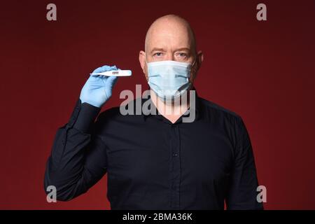 portrait d'un homme avec des gants, un masque et un thermomètre sur fond rouge Banque D'Images