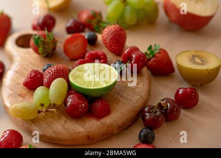 fruit de source coloré et délicieux sur table en bois avec lumière douce, fraises, bleuets, citron, lime, pomme, kiwi, cerise, raisin, tous frais et Banque D'Images