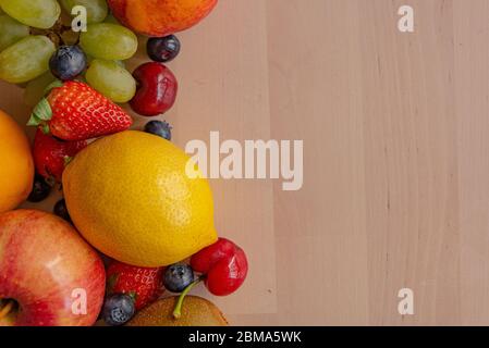 fruits de printemps sur table en bois à la lumière naturelle, fraises, bleuets, citron, lime, cerise, raisin, tous frais et mûrs, à la lumière douce Banque D'Images