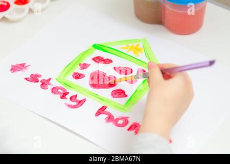 L'enfant dessine des coeurs rouges à l'intérieur de la maison sur une feuille de papier blanche avec les mots rester à la maison. Concept de séjour à la maison. Créativité des enfants. Banque D'Images