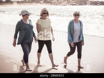 Un groupe de trois femmes âgées actives sur la marche des années 60, s'entraîner et s'amuser sur la plage. Les femelles matures rient en marchant en vacances Banque D'Images