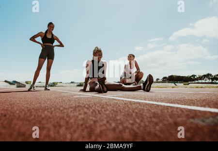 Les athlètes féminins prennent une pause après l'entraînement assis sur la piste de course dans le stade. Les femmes se détendent et sourient après l'entraînement. Banque D'Images