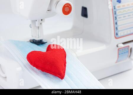Cœur rouge sur le masque. Les soins de santé et le coronavirus protègent avec un masque de couture. Couture de masques médicaux pour protéger contre le coronavirus.production de ma Banque D'Images
