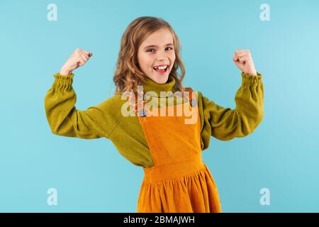 Photo d'une jeune fille blonde amusante montrant ses biceps et souriante isolée sur fond bleu Banque D'Images