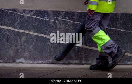 Un employé de Cleseup nettoie le sol en béton public avec un aspirateur. Les travailleurs portent un uniforme utiliser un souffleur de feuilles nettoyer le trottoir dans la ville. Nettoyage de la poussière par le concierge Banque D'Images