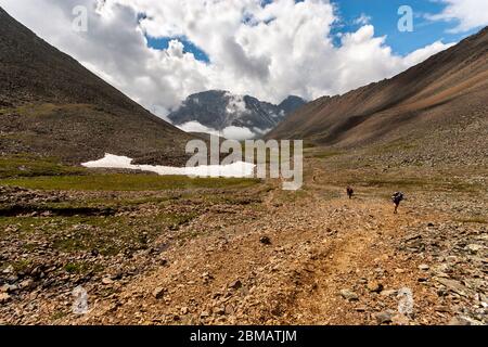 Plusieurs routards marchent le long d'un sentier de montagne rocheux. Grandes montagnes en arrière-plan dans les nuages. Pas de neige fondue sur le sol. Horizontale. Banque D'Images