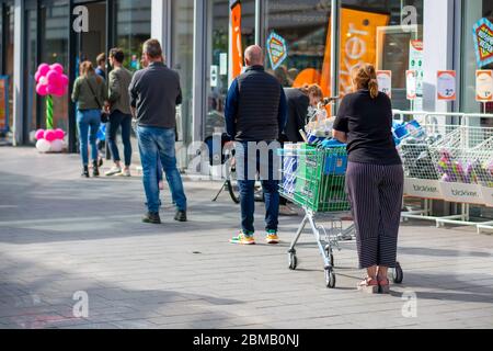 Les clients font la queue en dehors, ils font la distanciation sociale. Les gens qui attendent en ligne en gardant la distance sociale nécessaire de 1,5 mètres, à l'extérieur d'un supermarché Banque D'Images