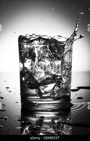 verre d'eau avec éclaboussures de la chute de glace cube, photographie noir et blanc . Banque D'Images