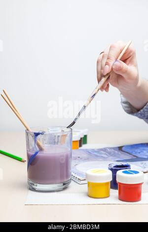 Un cliché vertical dans un studio d'art thérapie d'une main femelle tenant un pinceau et l'trempant dans un verre d'eau dans lequel une aquarelle a été dissoute Banque D'Images