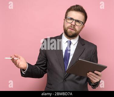 Un homme d'affaires sérieux en costume travaille avec une tablette et un stylet, fait un rapport ou une présentation, et regarde la caméra de manière inquissante. Banque D'Images