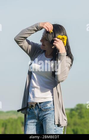 une belle fille, une brunette, se tient dans un pré de fleurs et ajuste les pissenlits dans ses cheveux Banque D'Images