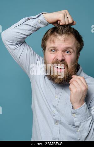 Un homme avec une barbe et une coiffure déchiquetés est énervé qu'il n'a pas visité un barbershop depuis longtemps en raison d'une pandémie. Banque D'Images