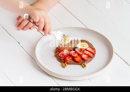 Crêpe hibou créative pour enfants dans une assiette isolée sur fond blanc. Un enfant à la fourchette prend une crêpe. Petit déjeuner végétarien sain, déjeuner Banque D'Images