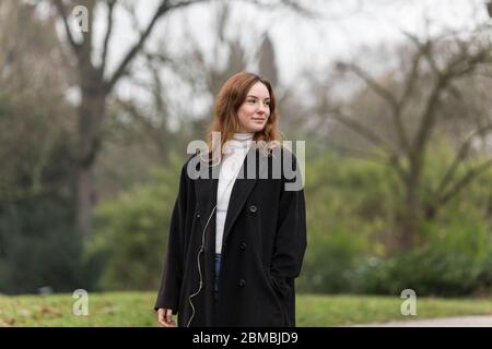 Jeune femme en long manteau de laine noir qui regarde loin dans le parc public Banque D'Images