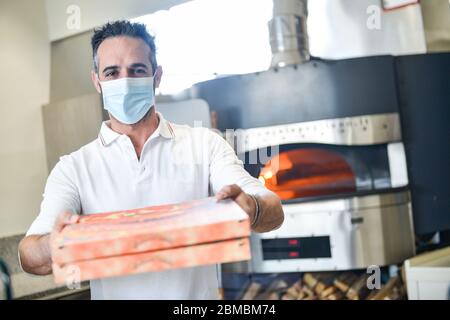 Pizzachef portant un masque sanitaire sert de la pizza à emporter Banque D'Images