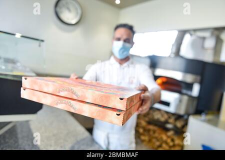 Pizzachef portant un masque sanitaire sert de la pizza à emporter Banque D'Images