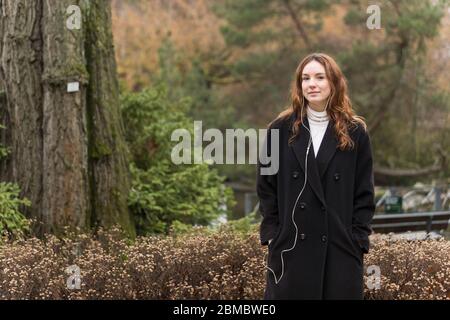 Jeune femme en manteau long noir regardant l'appareil photo Banque D'Images