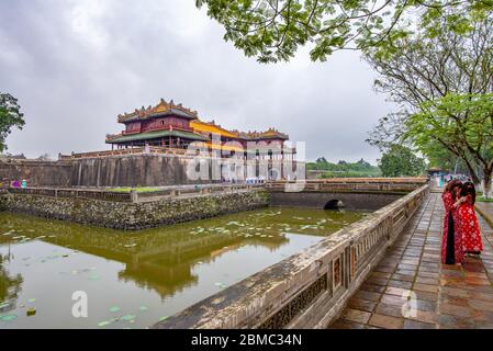 Hue, Vietnam - 15 avril 2018 : deux filles portant des vêtements traditionnels devant la porte principale de la citadelle de Hue, avec un ciel couvert Banque D'Images