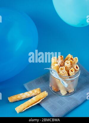 De savoureux petits pains à gaufres avec sucre glace dans un bol en verre avec des bulles sur fond bleu Banque D'Images