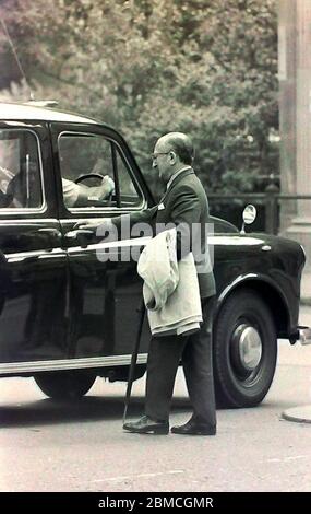 Un homme de haut rang en costume se met en taxi ou en taxi hackney dans une rue de Manchester, Angleterre, Royaume-Uni en 1974. Banque D'Images