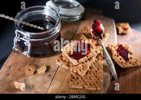 Ouvrez le bol contenant de la confiture de cassis sur une planche à découper en bois. Les biscuits secs se répartissent avec de la confiture, de la chapelure et une cuillère dans la confiture. Espace pour le texte. Banque D'Images