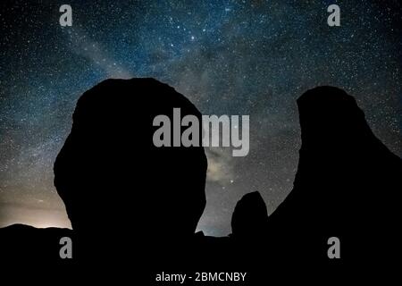 Ciel étoilé et voie lactée avec des nuages plus éclairés par des lumières de la ville éloignées, vues au-dessus des formations rocheuses dans le parc national de City of Rocks, situé entre-deux Banque D'Images