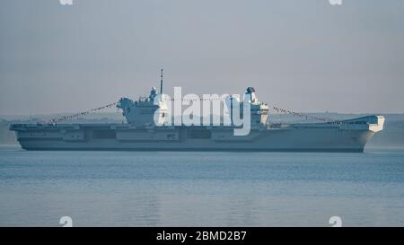 Le porte-avions de la Marine royale HMS Queen Elizabeth à l'ancre dans le Solent, au large de l'île de Wight, au Royaume-Uni, dans la soirée du 8 mai 2020. Malgré le blocage national du coronavirus, le navire est habillé de façon générale pour commémorer le 75e anniversaire de la fête de la VE. Banque D'Images