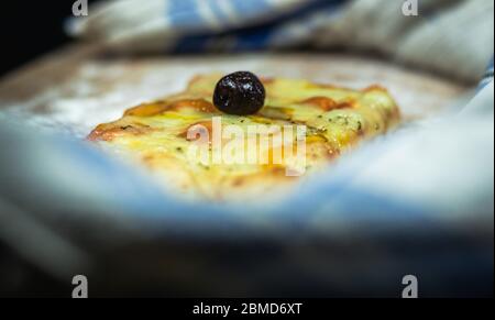 Pizza à pain plat au fromage et olives noires sur une planche à découper avec de la farine entourée d'une serviette en fond noir Banque D'Images