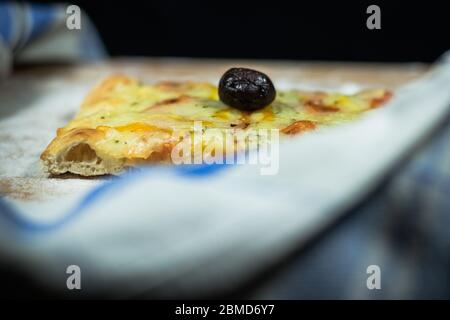 Pizza à pain plat au fromage et olives noires sur une planche à découper avec de la farine entourée d'une serviette en fond noir Banque D'Images