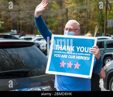 Un professionnel de la santé portant un masque et des exfoliants, agitant les gens alors qu'il tient un panneau remerciant nos héros, pendant la semaine nationale des infirmières. Banque D'Images