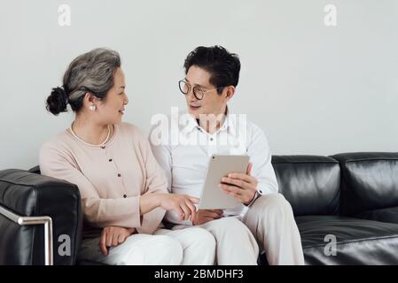 Un couple asiatique âgé utilisant des appareils électroniques sur le canapé Banque D'Images