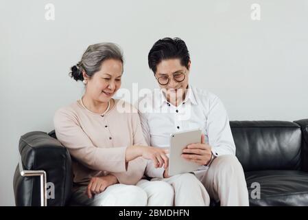 Un couple asiatique âgé utilisant des appareils électroniques sur le canapé Banque D'Images