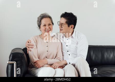 Un couple asiatique âgé utilisant des appareils électroniques sur le canapé Banque D'Images