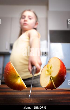 Une jeune fille fière coupe la pomme rouge en deux à la maison dans la cuisine Banque D'Images