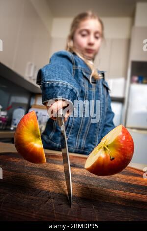 Une fille caucasienne coupe la pomme rouge en deux à la maison dans la cuisine. Mise au point peu profonde. Banque D'Images